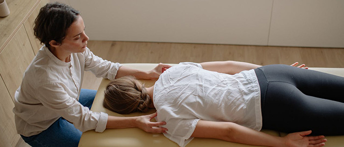A woman lying face-down and a chiropractor working on her shoulders