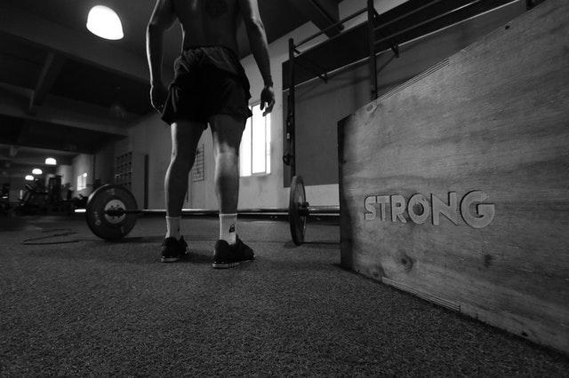 A photo of a muscular person standing alone in the gym next to a sign saying Strong, symbolizing reasons to consider hiring a personal trainer